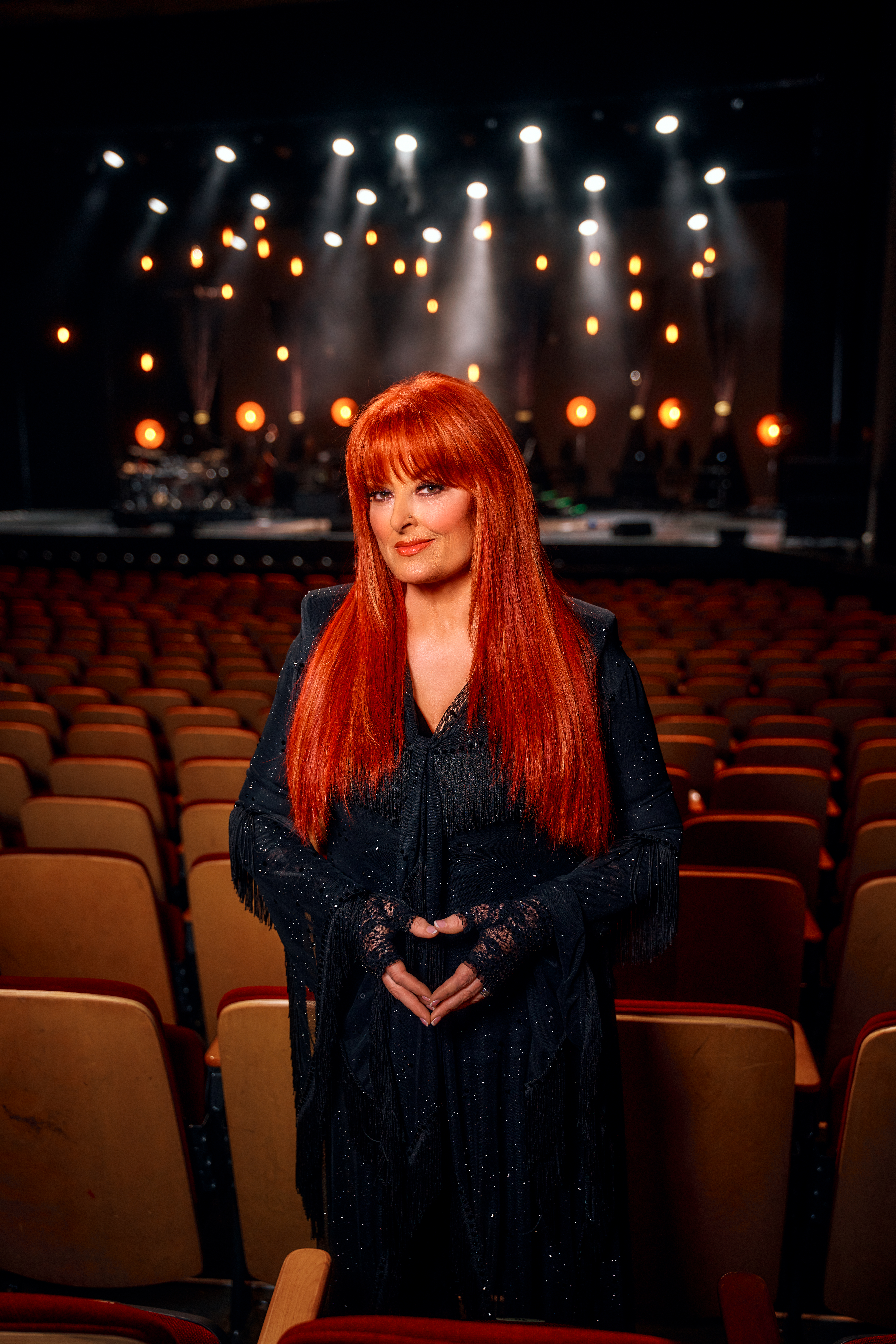 A photo of Wynonna Judd with red hair and a black dress, standing in a theatre