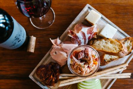 a charcuterie board filled with spreads, meats, and cheese with a bottle and glass of red wine