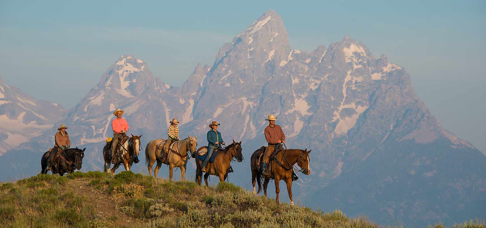 a group of people horseback riding with mountains behind them in Jackson Hole