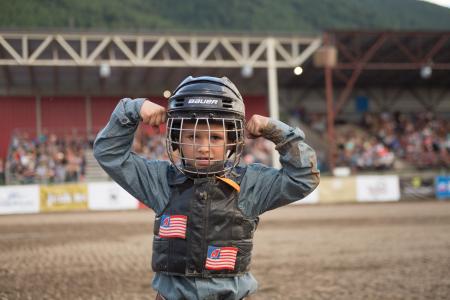 A young child flexes their muscles while wearing a rodeo helmet and vest in Jackson Hole, WY.