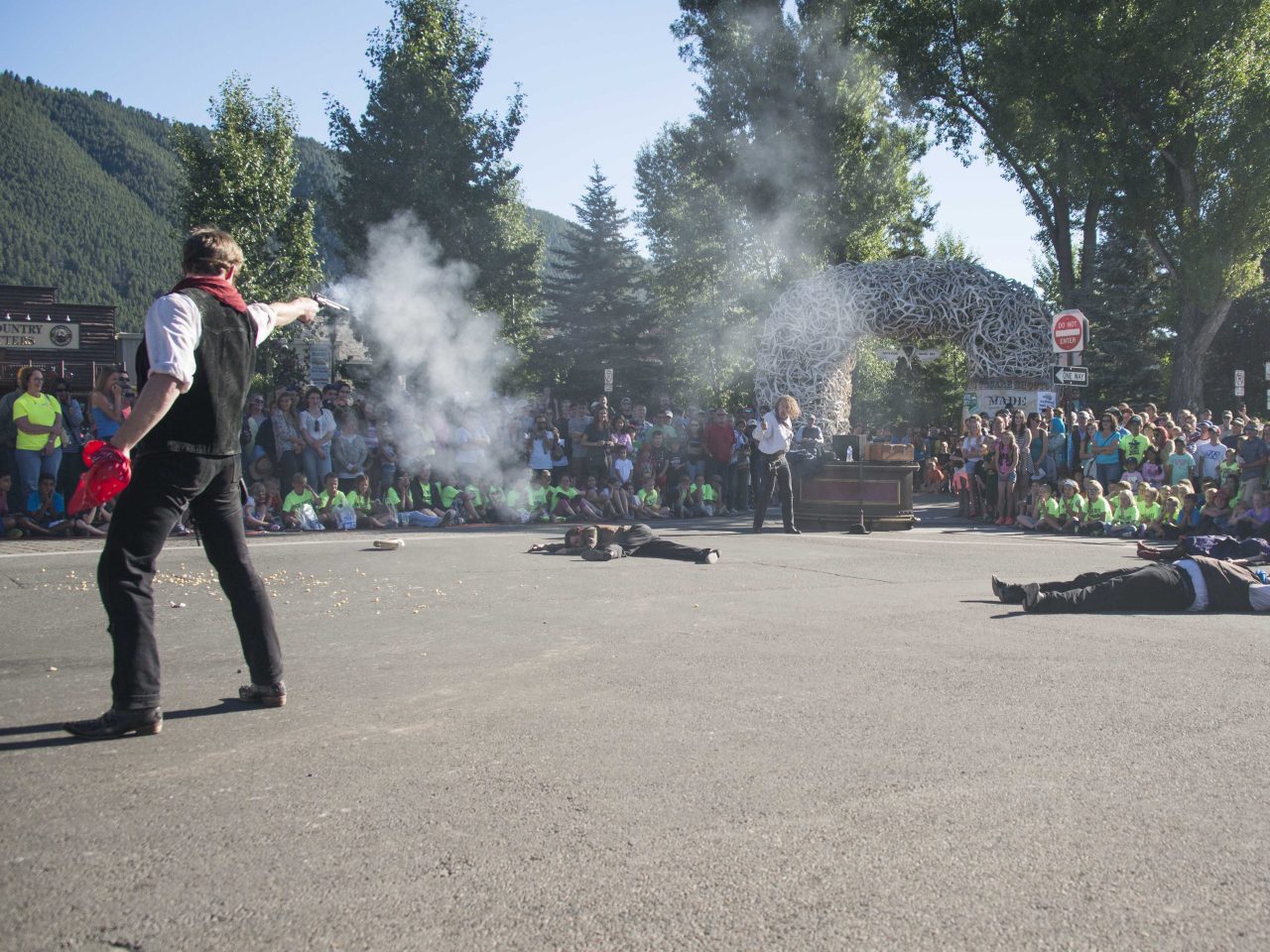 families watch as an actor shoots a gun as other actors lay on the ground during the Jackson Hole Shoot Out