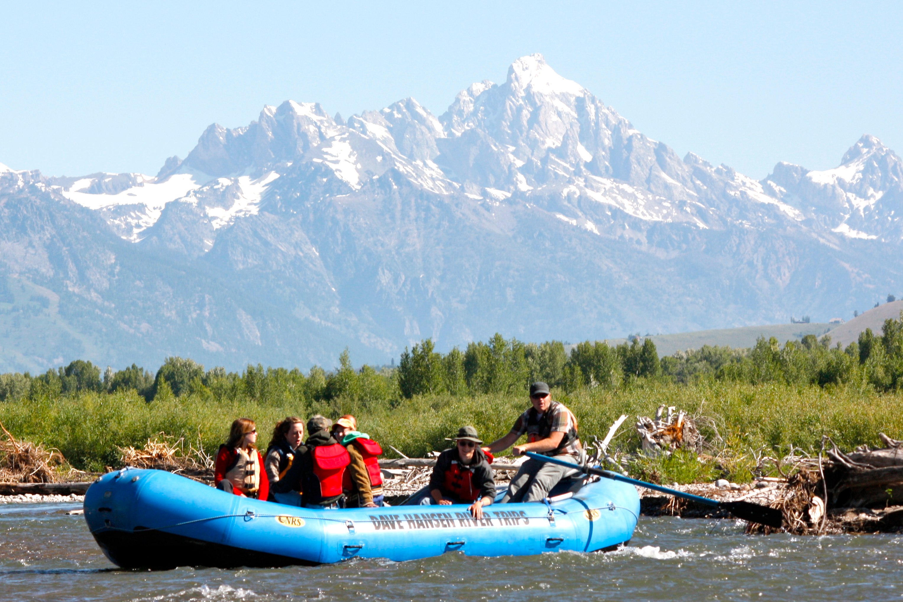 a family rafts along a river while enjoying scenic views of mountains in Jackson Hole