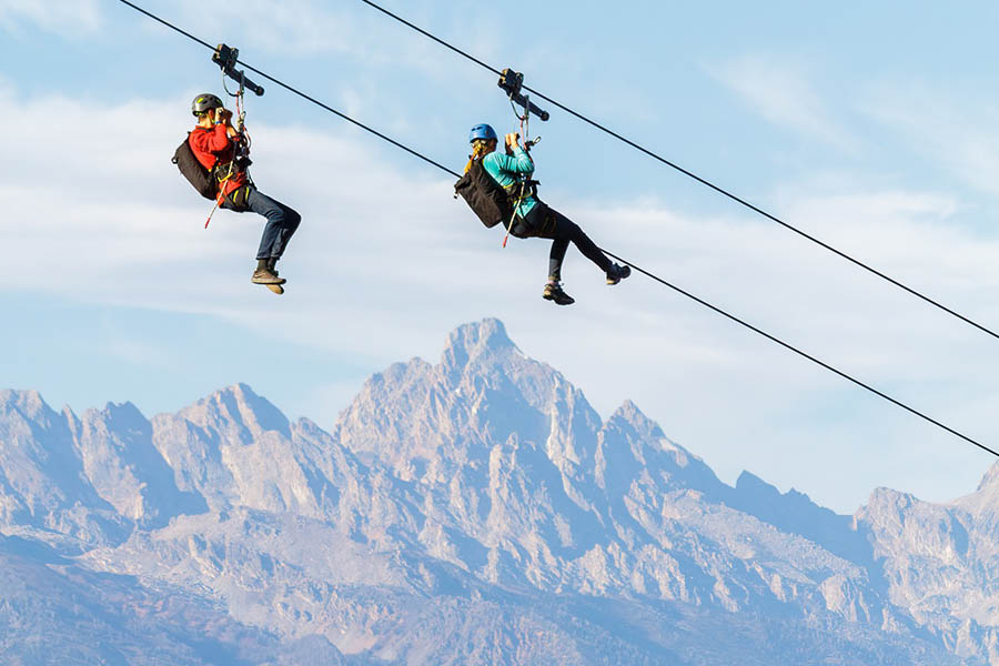 a man and woman zipline while enjoying mountain views in Jackson Hole, WY