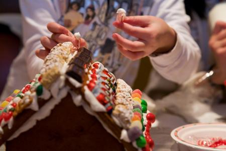 close up of people decorating the roof of a gingerbread house with different candies