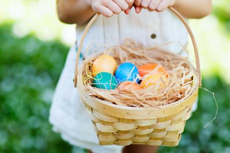 A child holds an Easter basket filled with multicolored Easter eggs.