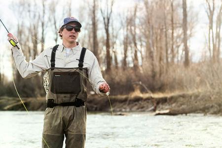 An angler stands in a stream and casts a fishing line in Jackson Hole, WY.